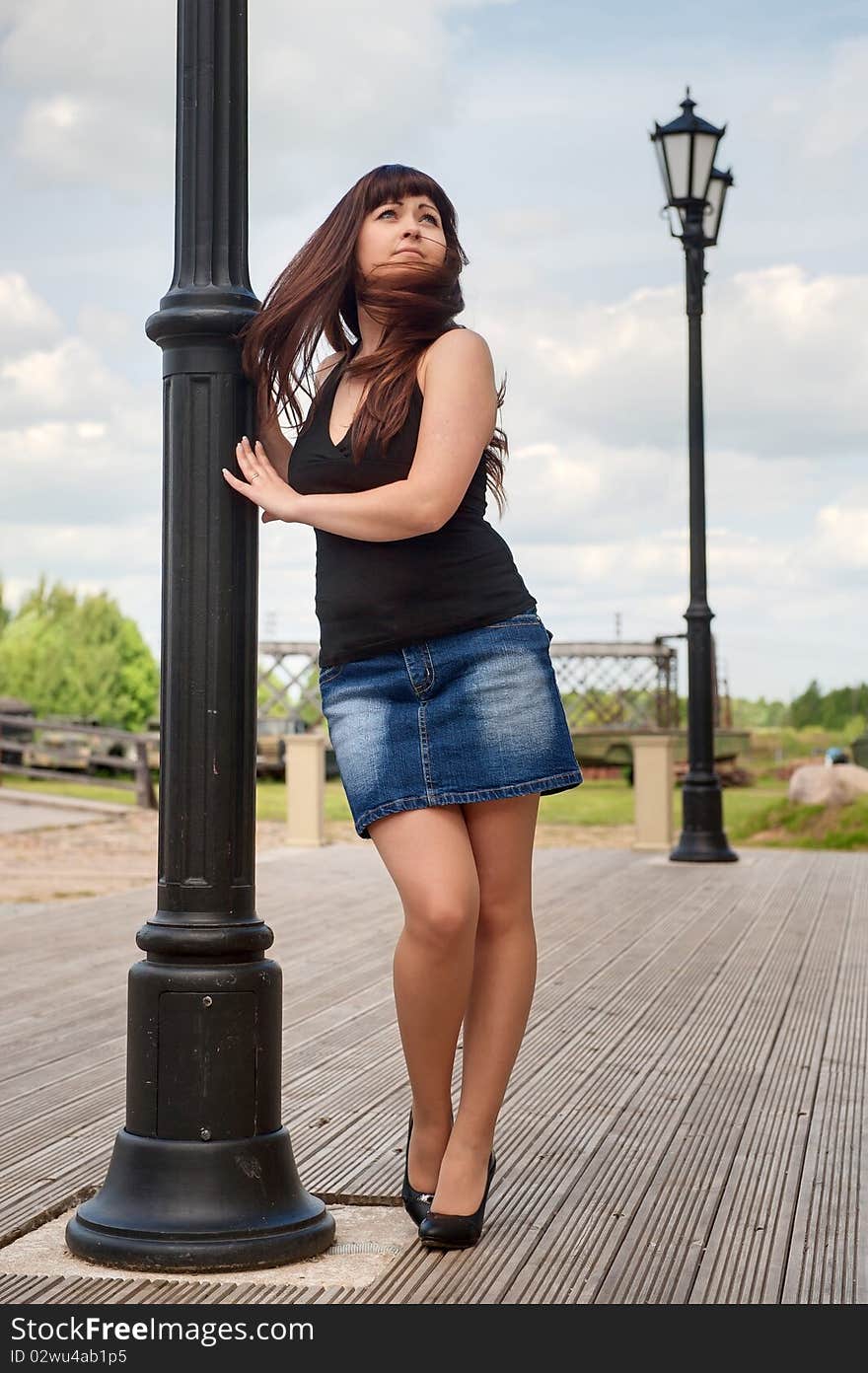 Young, woman in short skirt leans on lantern pillar and looks upwards. Young, woman in short skirt leans on lantern pillar and looks upwards.