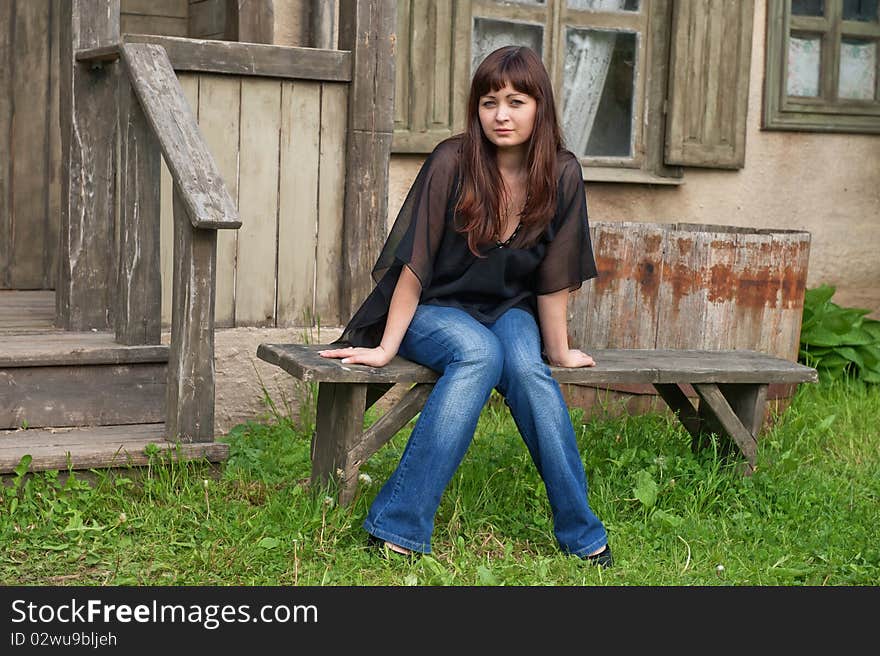 Young beautiful woman sit on the bench in front of old house. Young beautiful woman sit on the bench in front of old house.