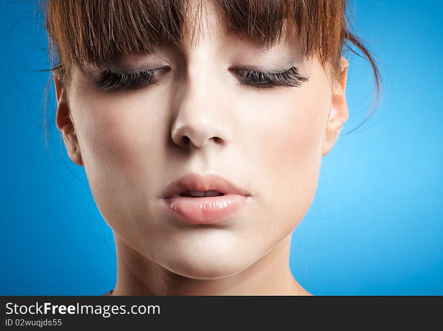 Isolated young woman looking downwards, on blue background