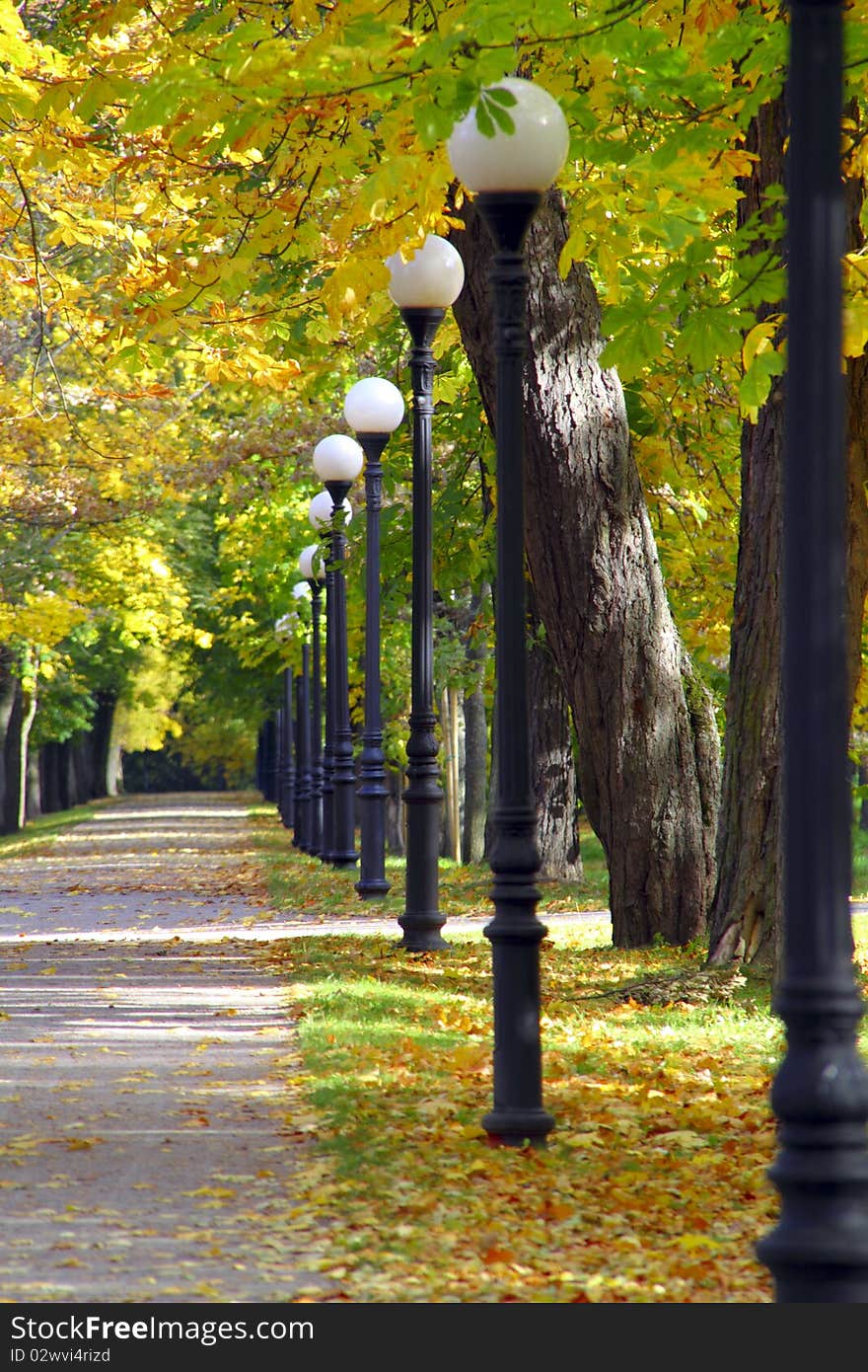 Sunny day in park during fall, alley with metal post lamps. Sunny day in park during fall, alley with metal post lamps