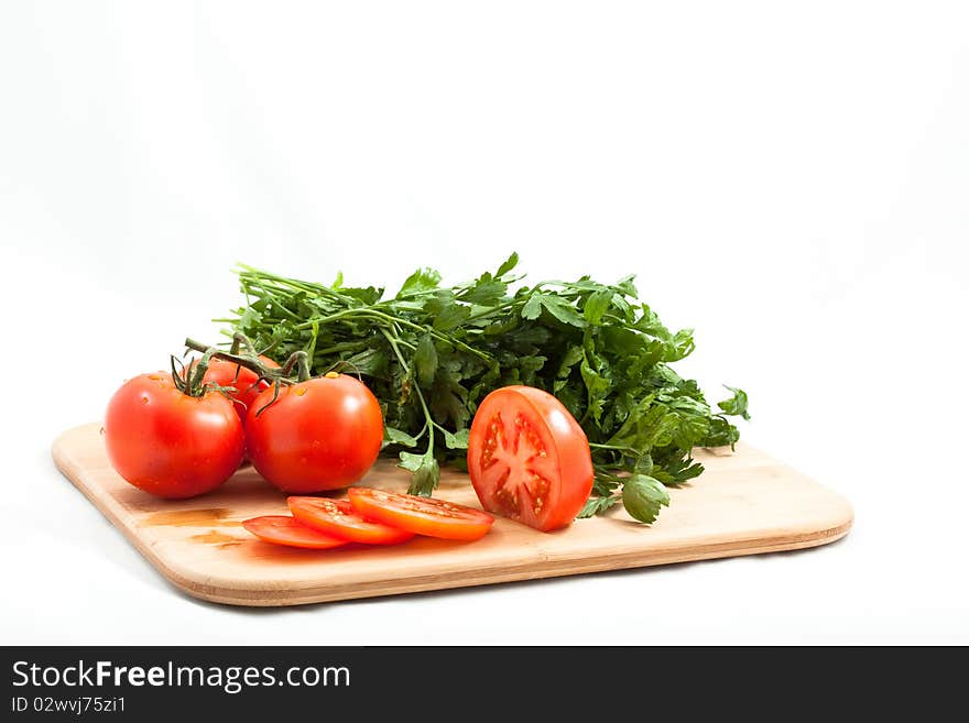 Fresh tomatos tomatoes sliced on a bamboo cutting board with italian parsely in the background. Close crop isolated on white. Fresh tomatos tomatoes sliced on a bamboo cutting board with italian parsely in the background. Close crop isolated on white