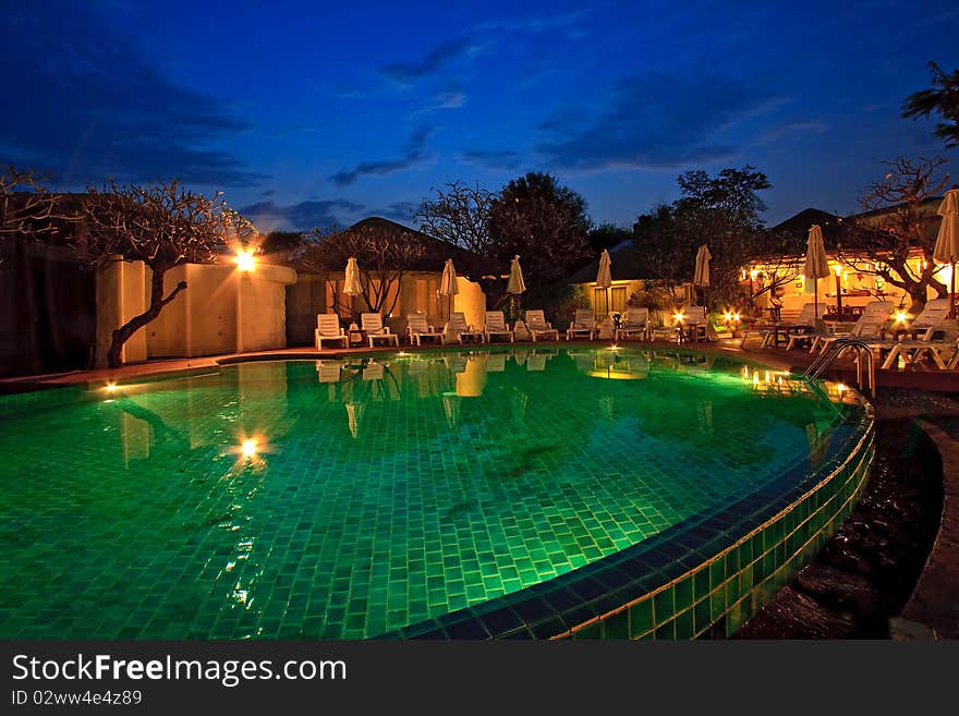 Lounge chairs and Umbrella surround a swimming pool at dusk