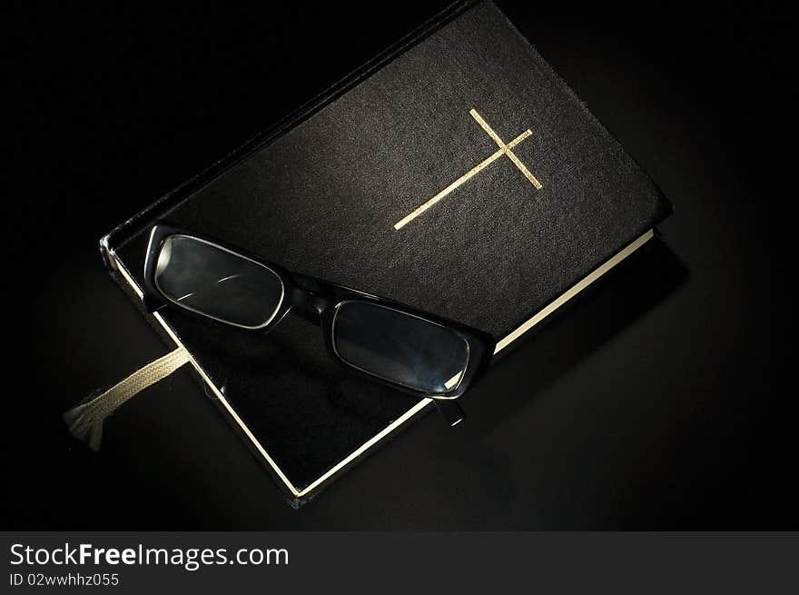 Bible with eyeglasses. Black background