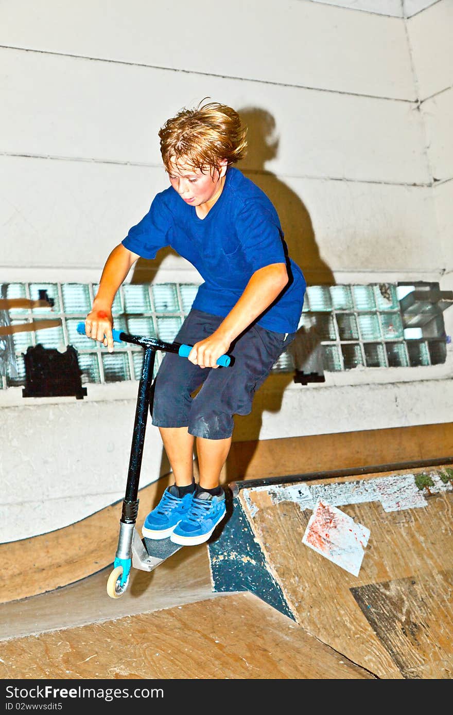 Boy goes airborne with his scooter in the skate hall