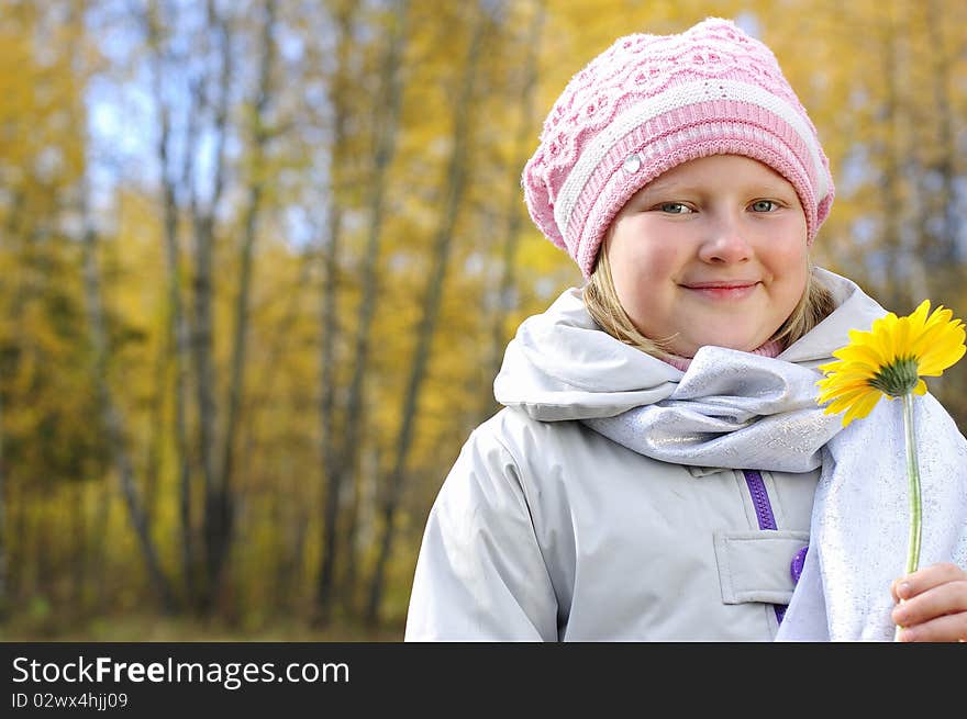 A little girl with a yellow flower in the autumn forest. Portrait.