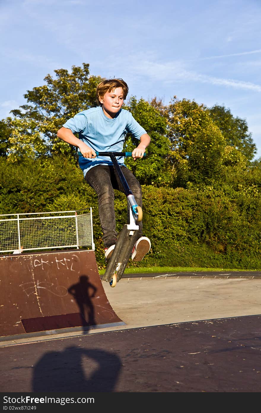 Boy jumps with scooter at the skate park over a ramp and has fun