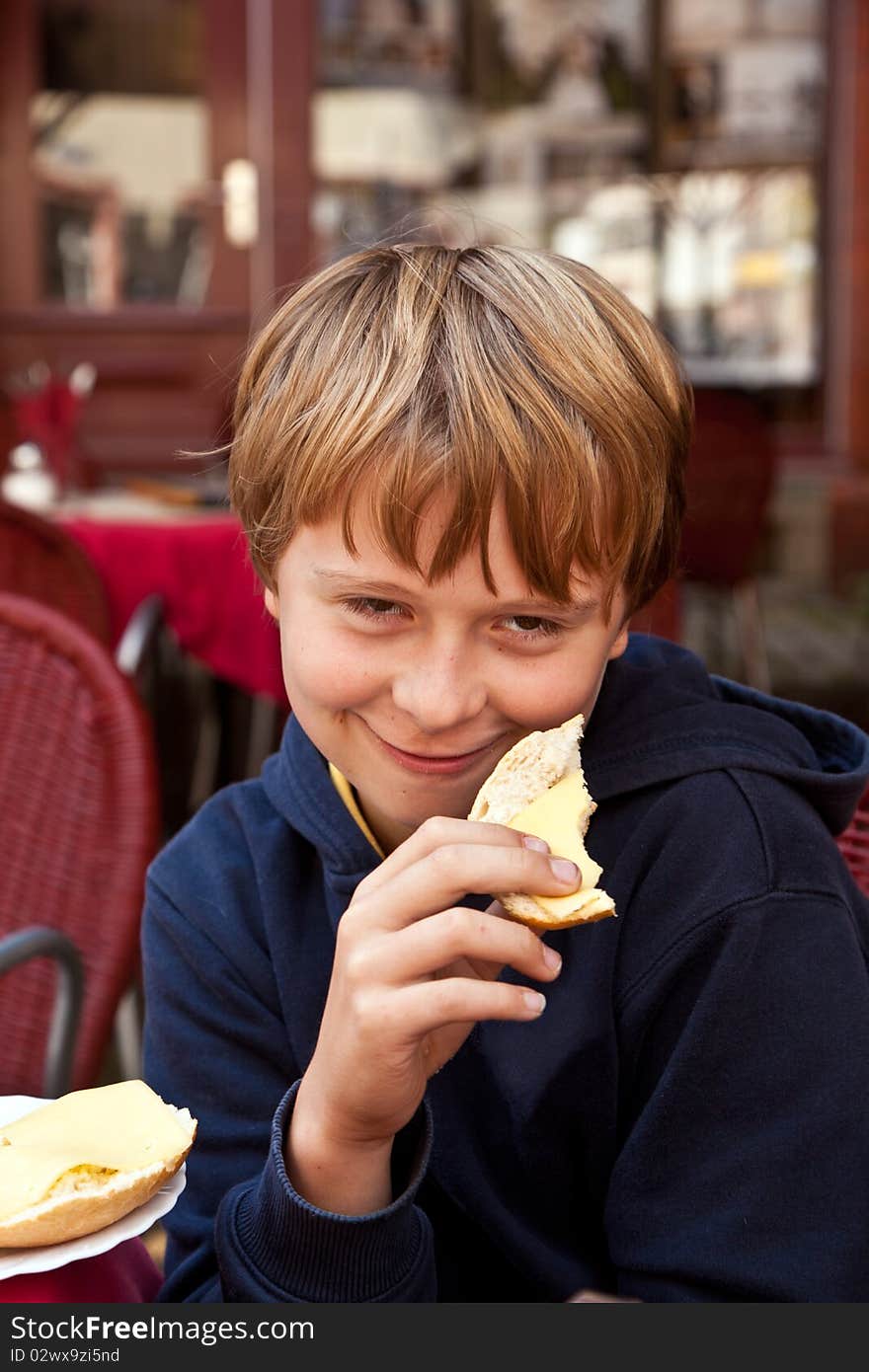 Portrait of a handsome smiling boy,sitting and eating a role outside