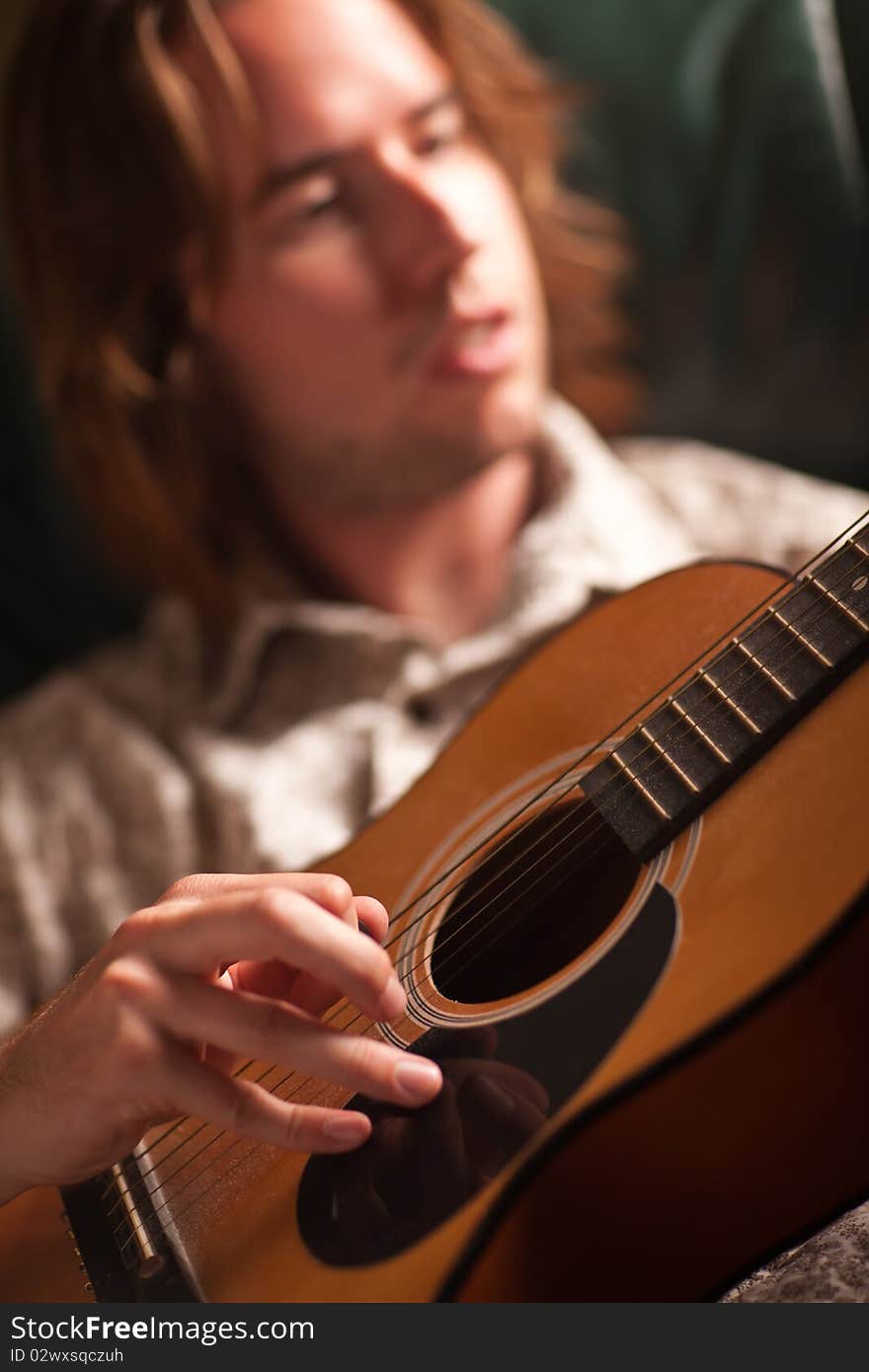 Young Musician Plays His Acoustic Guitar under Dramatic Lighting.