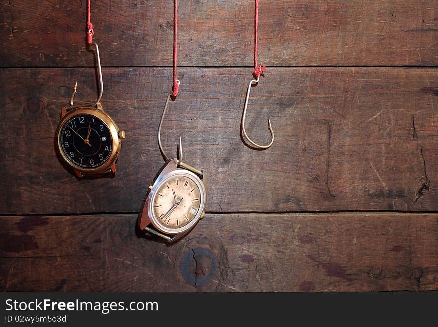 Two old watches hanging on fish hooks on wooden background. Two old watches hanging on fish hooks on wooden background