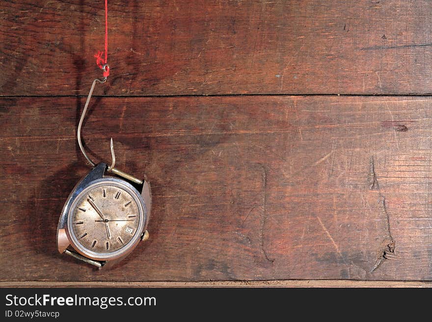 Old watch hanging on fish hook with red thread on wooden background. Old watch hanging on fish hook with red thread on wooden background