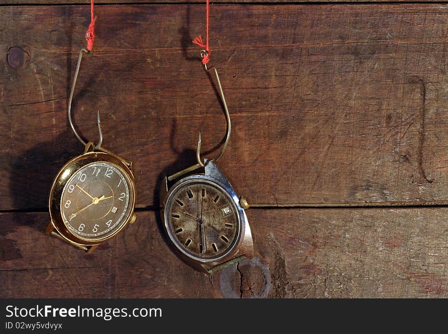 Two old watches hanging on fish hooks on wooden background. Two old watches hanging on fish hooks on wooden background