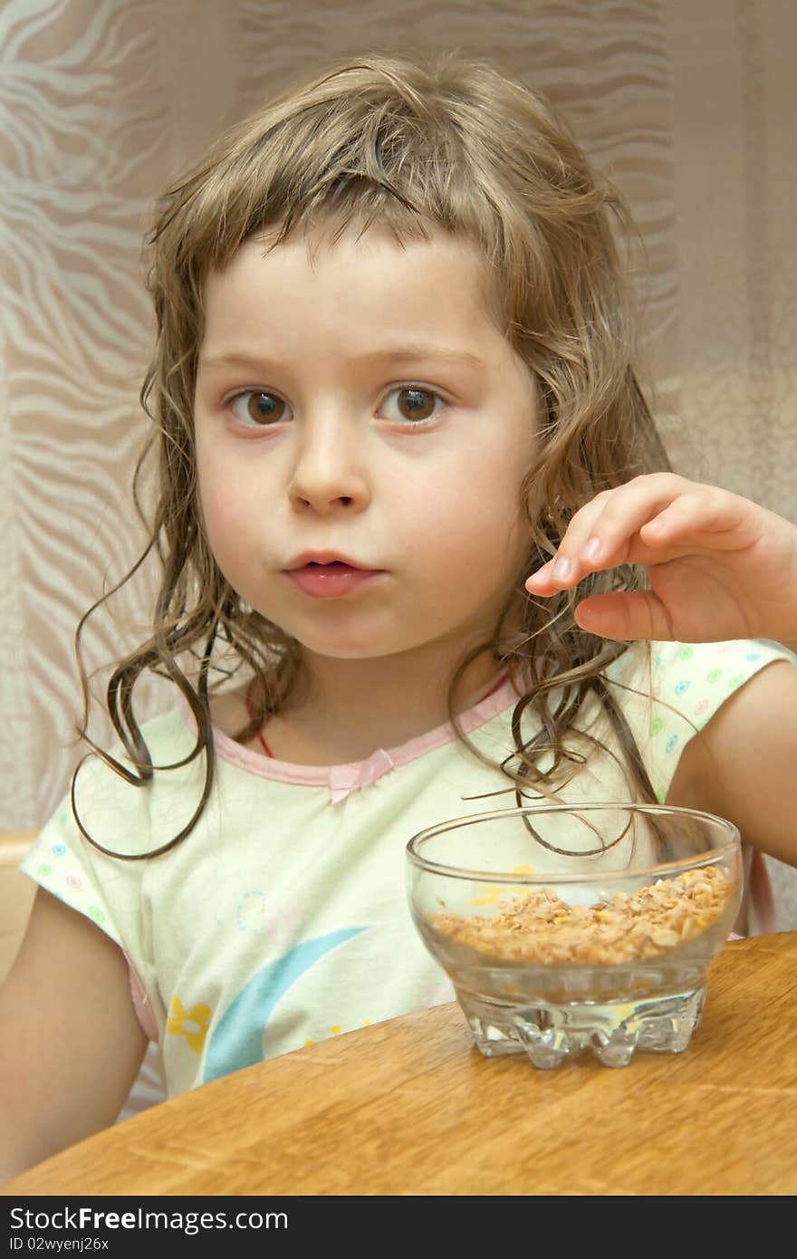 The thoughtful child sits at a table and wishes to take dry flakes from a dish