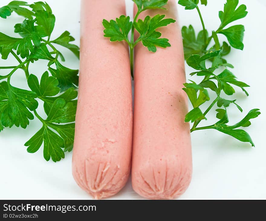 Two sausages on a white plate close up also are decorated by greens. Two sausages on a white plate close up also are decorated by greens