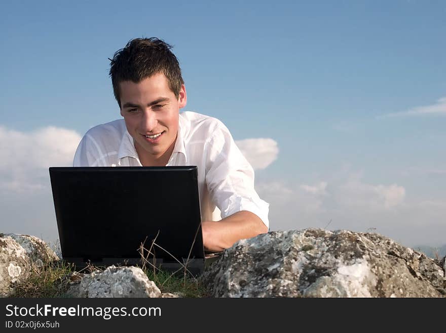 Young man using his laptop, sitting on the  rocky. Young man using his laptop, sitting on the  rocky