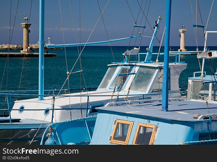 Typical Greek fishing boats are waiting in the harbor for departure. Two bronze deers guard the entrance to the Mandraki harbor. Typical Greek fishing boats are waiting in the harbor for departure. Two bronze deers guard the entrance to the Mandraki harbor.