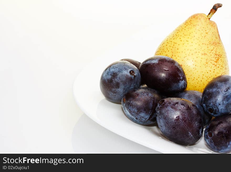 Fresh yellow pear on a white plate with plums