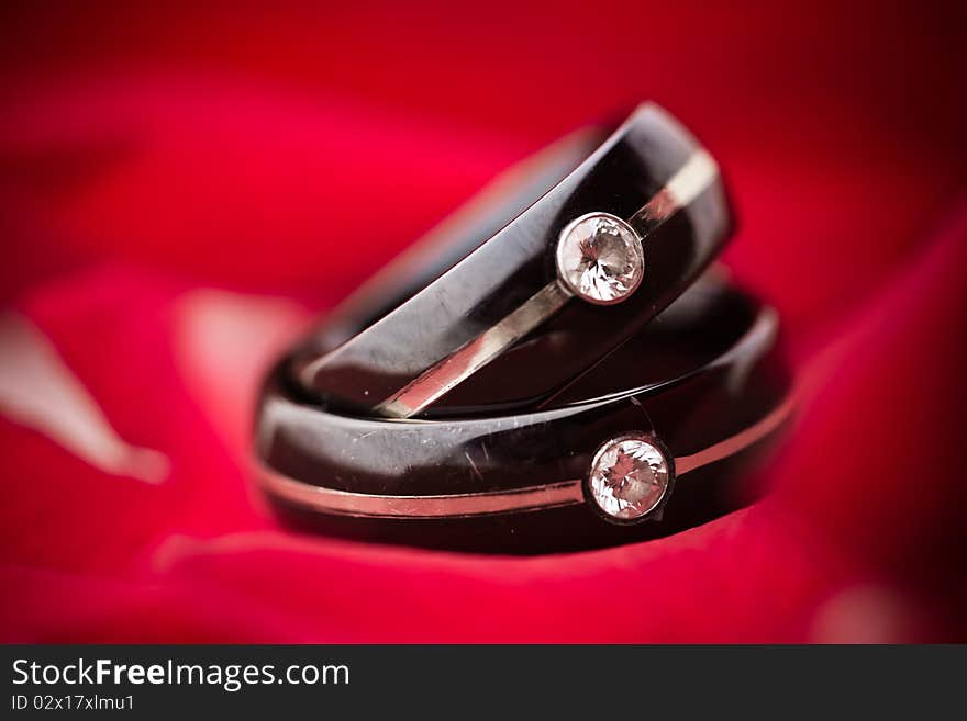 Dark black wedding diamond rings on red rose petal background. Dark black wedding diamond rings on red rose petal background