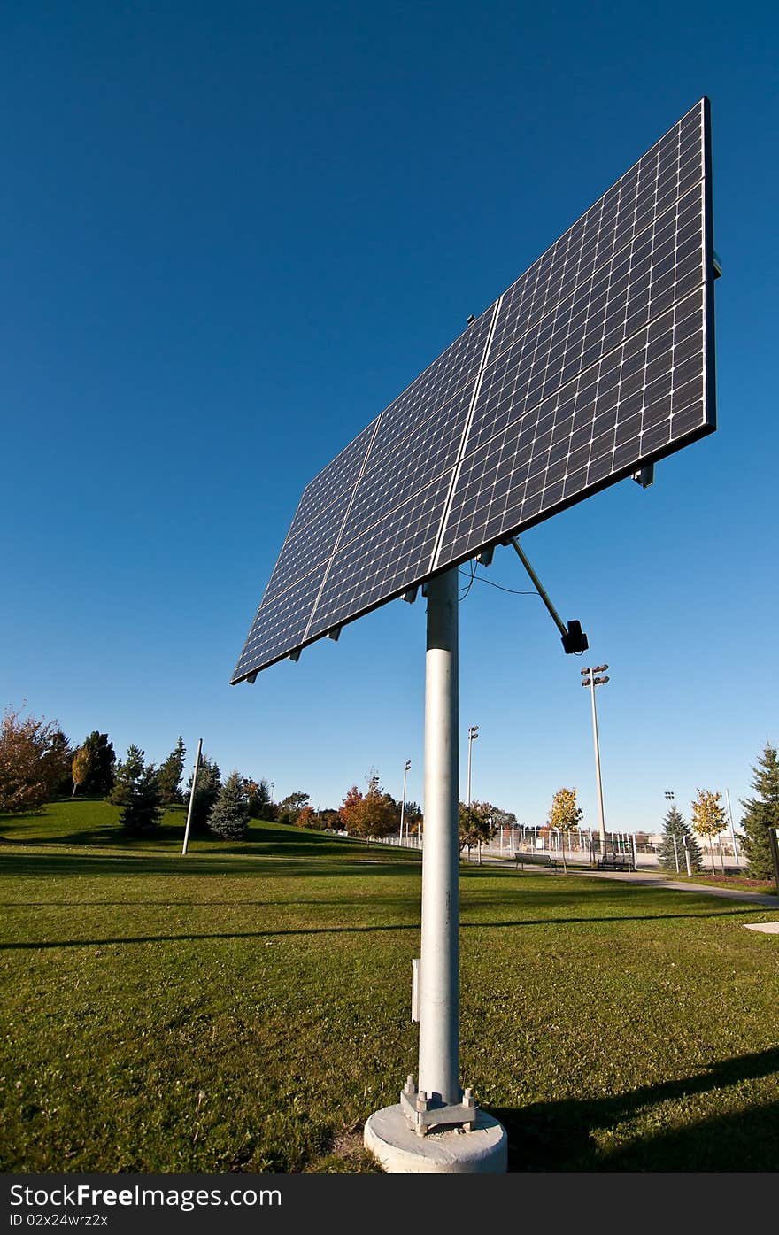 A photovoltaic solar panel array in a park with a blue sky in the background. A photovoltaic solar panel array in a park with a blue sky in the background.