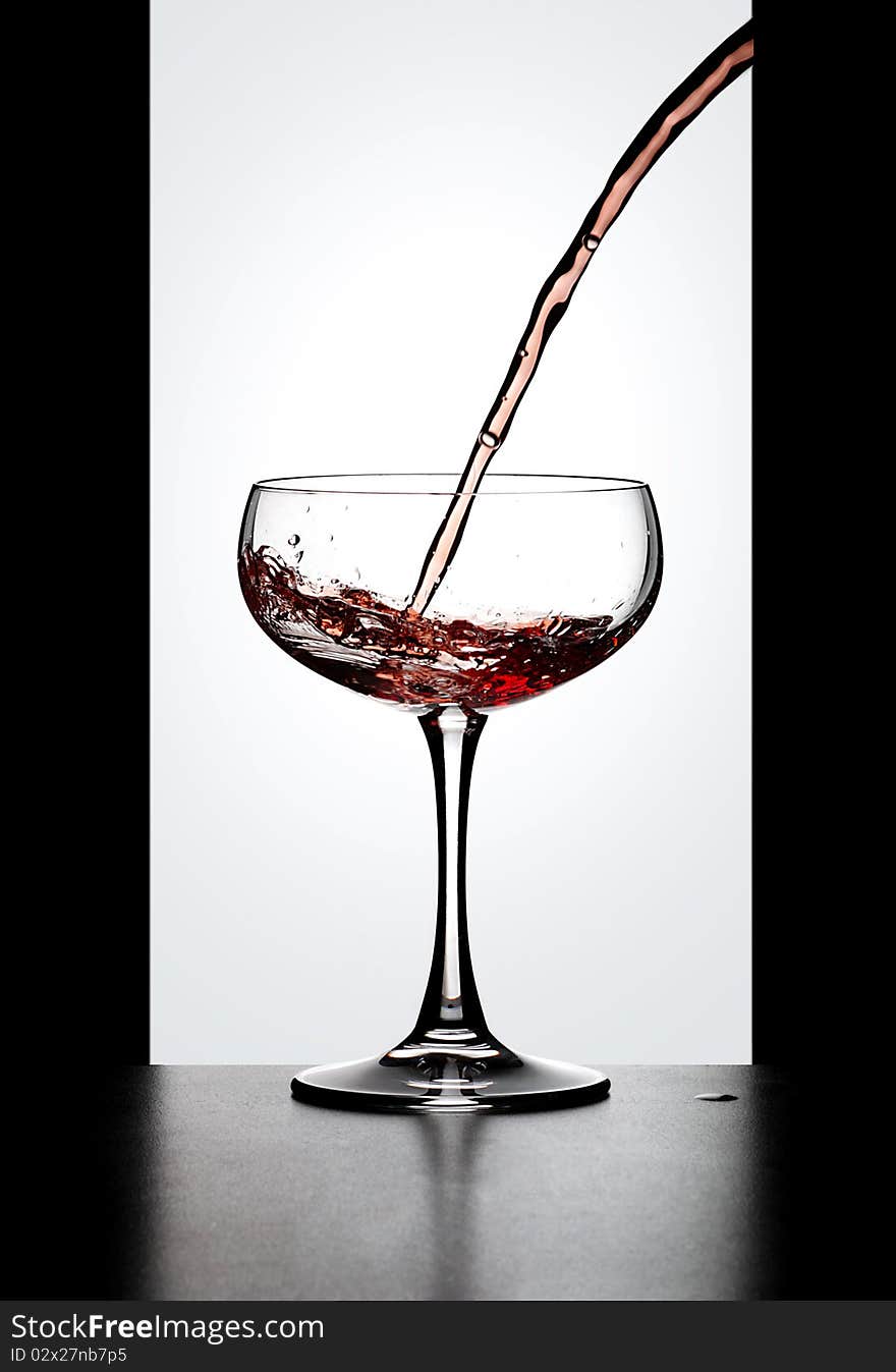 Dynamic action, red wine in glass bowl resting on a bench in front of a window. Dynamic action, red wine in glass bowl resting on a bench in front of a window