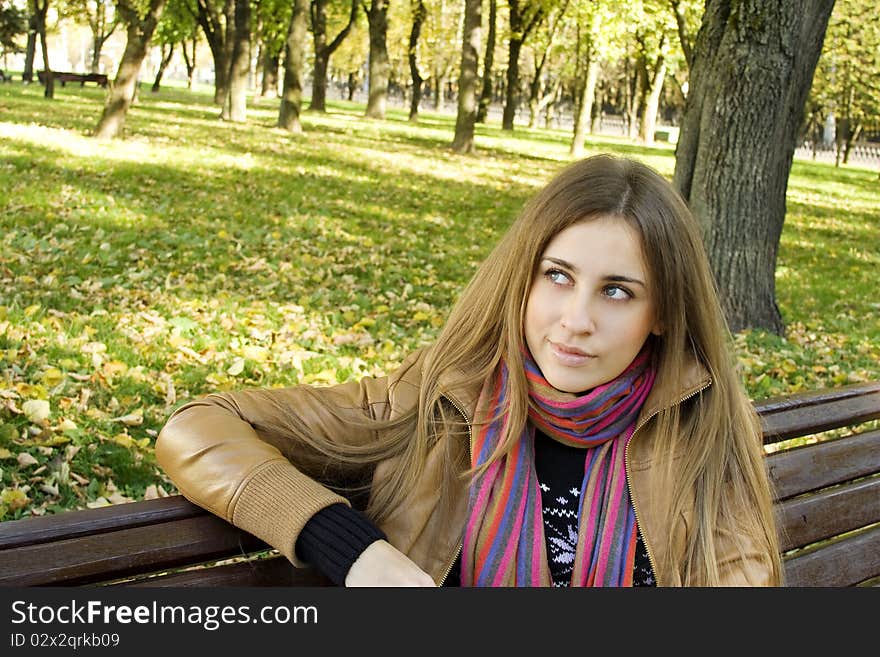 Horizontal portrait of a beautiful young woman sitting on a bench in the park around a lot of yellow, red green leaves. Horizontal portrait of a beautiful young woman sitting on a bench in the park around a lot of yellow, red green leaves.