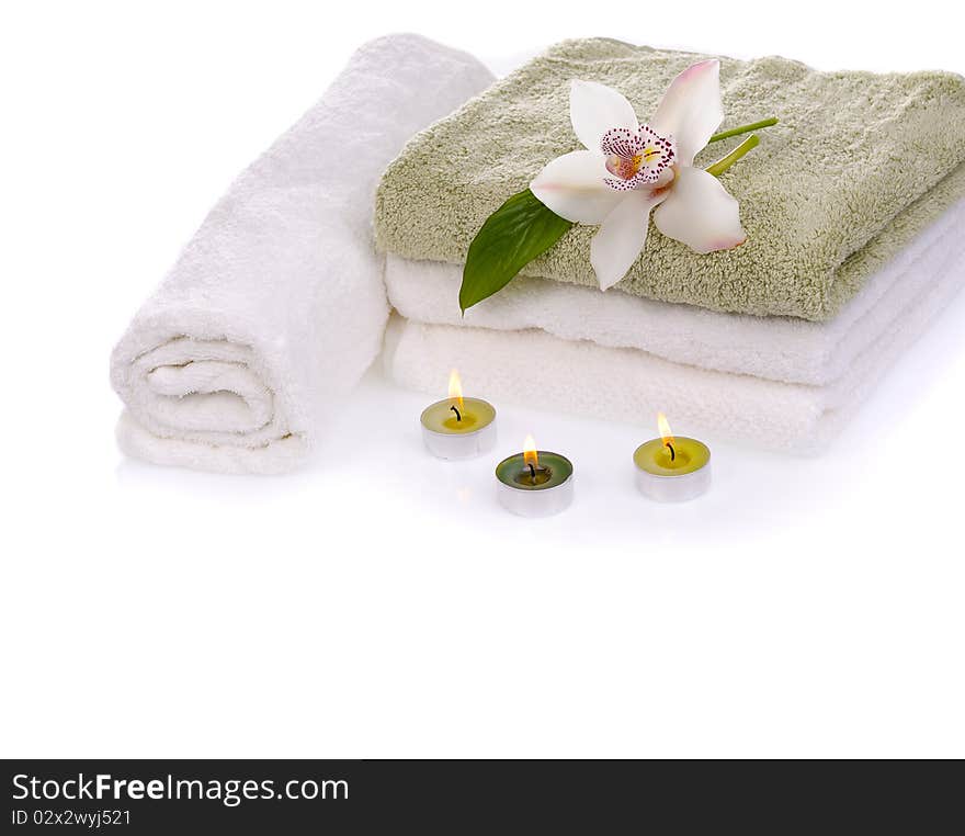 Stack of towels with white orchid flower and green burn scened candles isolated on white. Stack of towels with white orchid flower and green burn scened candles isolated on white