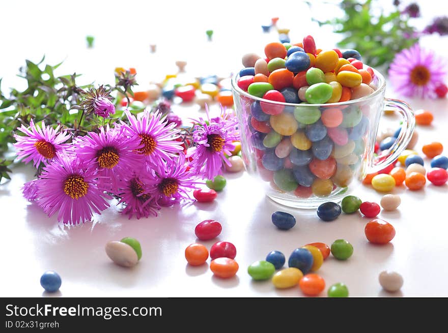 Varicoloured candies in a cup and pink flowers. Varicoloured candies in a cup and pink flowers