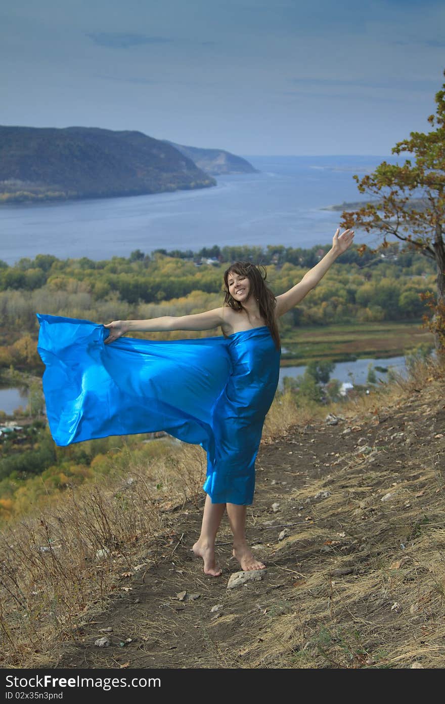 A young girl in a blue dress dancing on a mountain