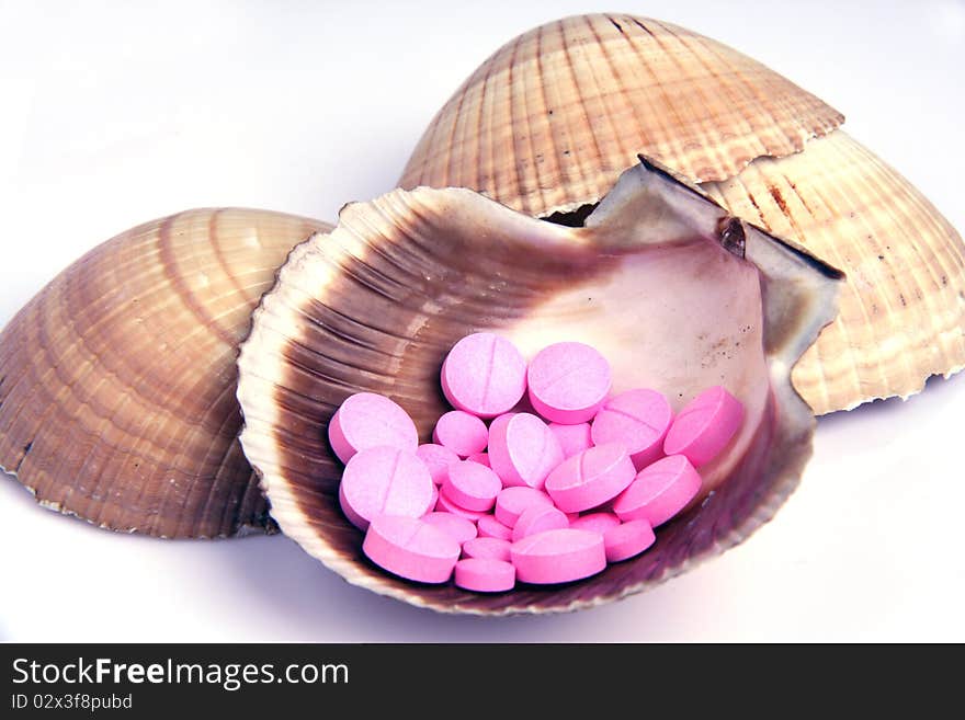 Pink pills of many sizes grouped together in a sea shell. Pink pills of many sizes grouped together in a sea shell