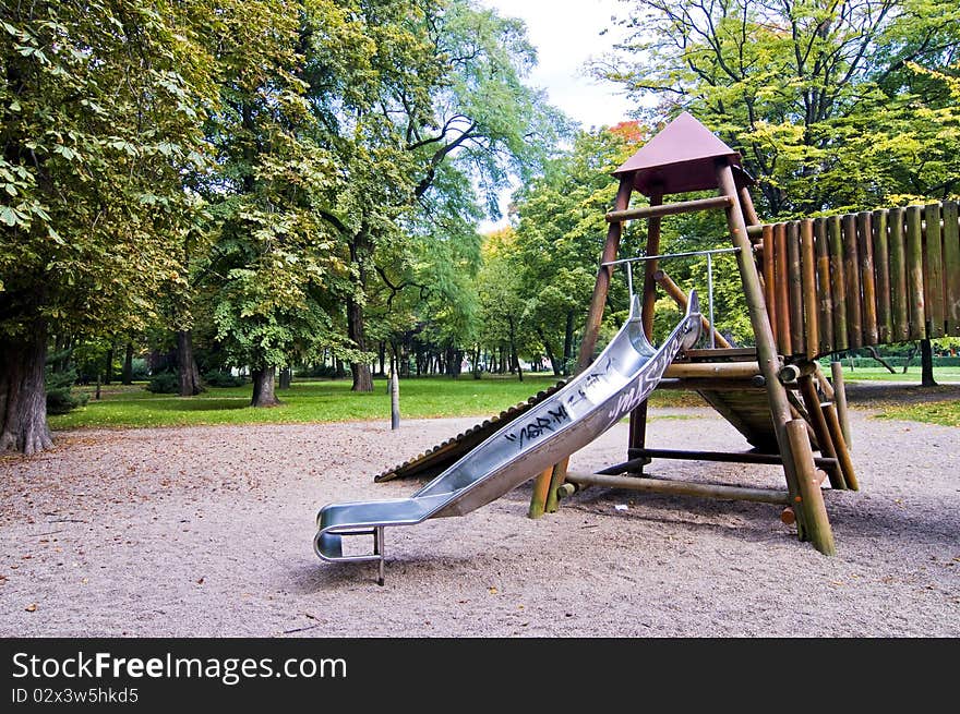 Slides in park during autumn, wide range of colors, green trees and yellow sand, wooden playground