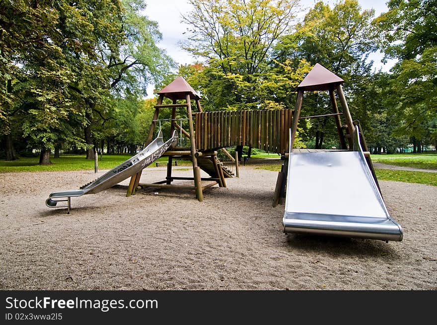 Slides in park during autumn, wide range of colors, green trees and yellow sand, wooden playground