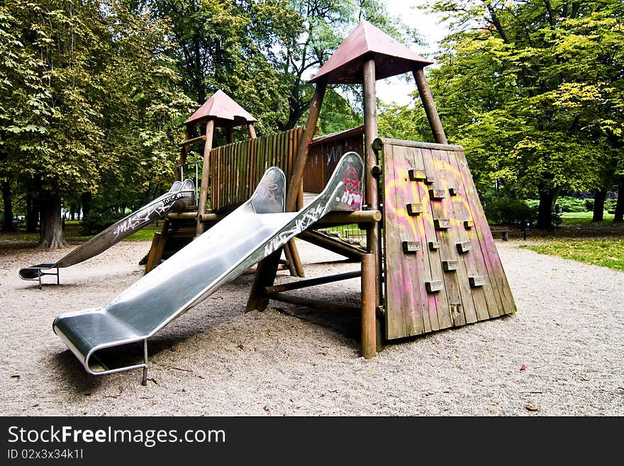 Slides in park during autumn, wide range of colors, green trees and yellow sand, wooden playground