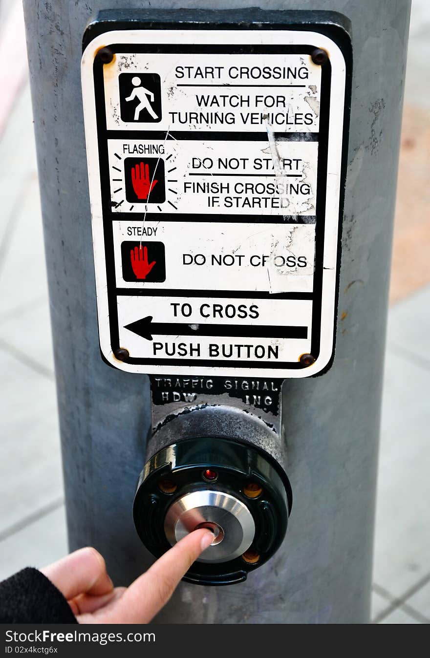 A finger pressing the button of a traffic light. A finger pressing the button of a traffic light