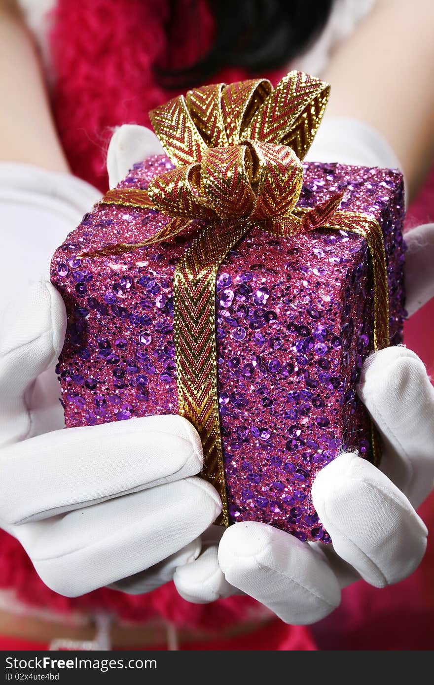 Sequence decorated christmas gift held by white gloves with holiday woman in background. Sequence decorated christmas gift held by white gloves with holiday woman in background.