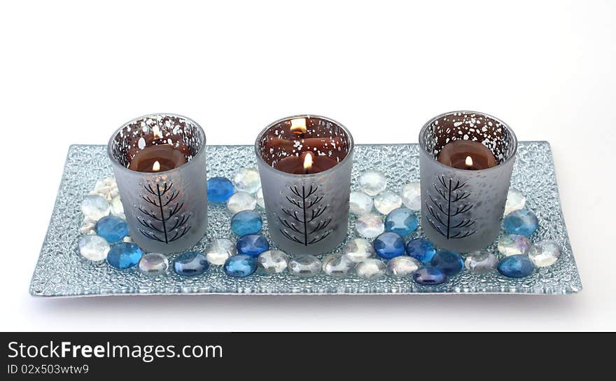 Three candles in decorative holders on a glass plate with coloured pebbles, over white. Christmas theme. Three candles in decorative holders on a glass plate with coloured pebbles, over white. Christmas theme.