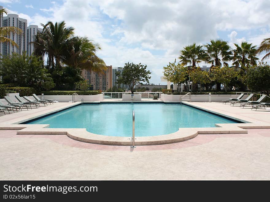 A swimming pool in the tropics surrounded by palm trees and sunshine.