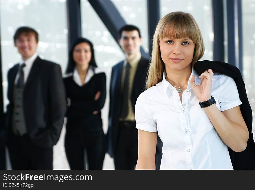 A young blond businesswoman in formal clothes in front of her colleagues. The image is taken on an abstract background. A young blond businesswoman in formal clothes in front of her colleagues. The image is taken on an abstract background.