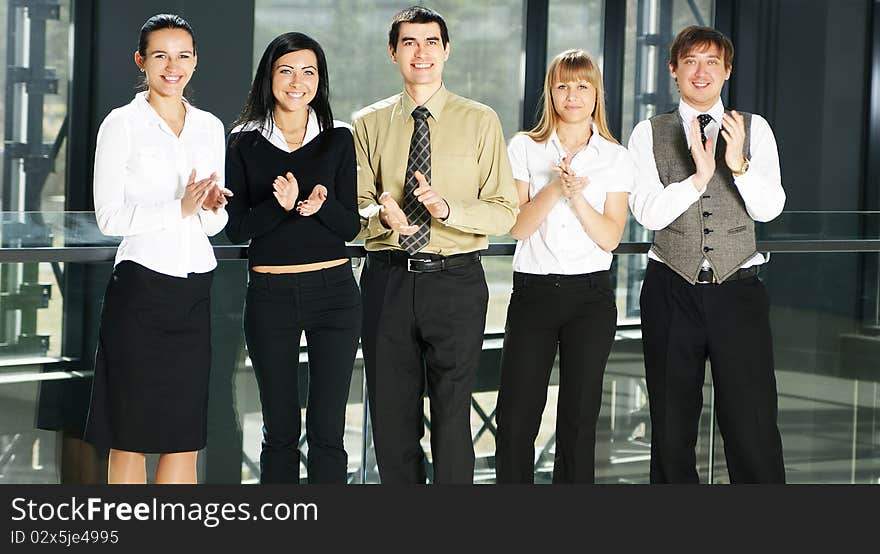 Five young businesspersons in formal clothes are clapping their hands. The image is taken on an office background. Five young businesspersons in formal clothes are clapping their hands. The image is taken on an office background.