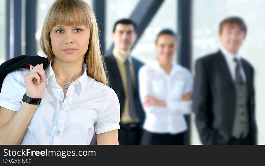 A young blond businesswoman in formal clothes in front of her colleagues. The image is taken in a modern office. A young blond businesswoman in formal clothes in front of her colleagues. The image is taken in a modern office.