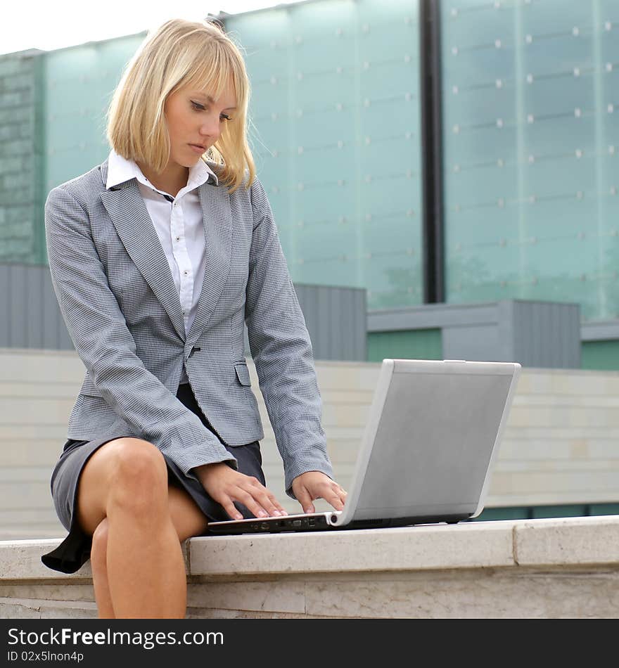 A young and smart businesswoman in formal clothes is working outdoors with a laptop. A young and smart businesswoman in formal clothes is working outdoors with a laptop.