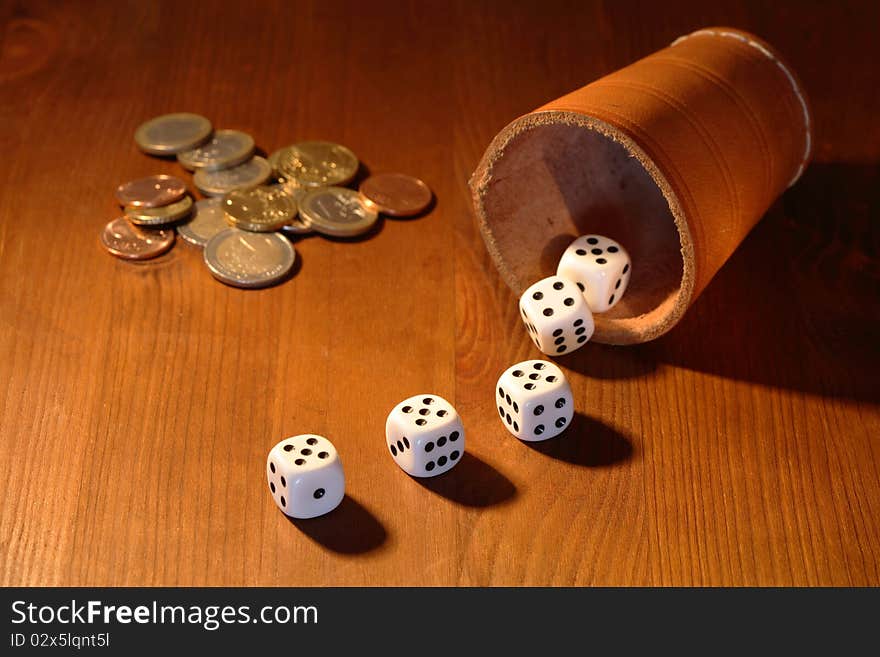 Five white dice and leather cup near coins lying on wooden background. Five white dice and leather cup near coins lying on wooden background