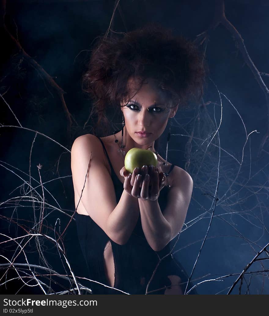 Fashion shoot of a young and attractive girl in a bizarre dress with a green apple. The image is taken on a mystique background with branches. Fashion shoot of a young and attractive girl in a bizarre dress with a green apple. The image is taken on a mystique background with branches.