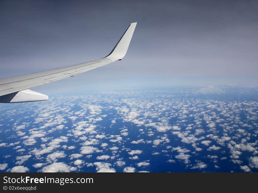 Plane wing in the sky with small clouds below and approaching darkness. Plane wing in the sky with small clouds below and approaching darkness