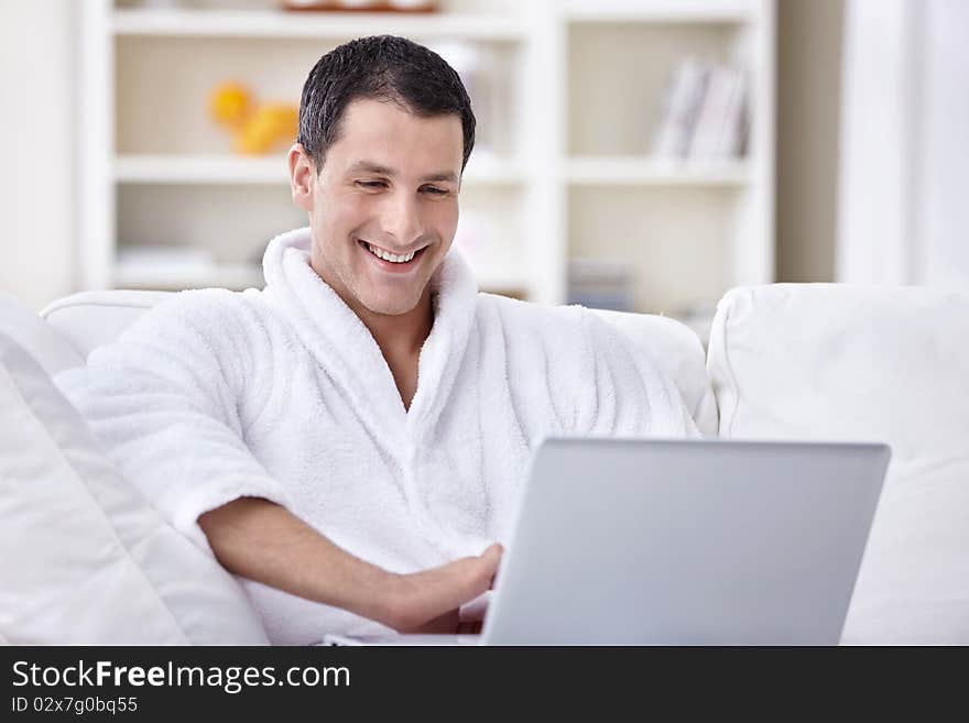 Laughing young man in a bathrobe looking at laptop. Laughing young man in a bathrobe looking at laptop