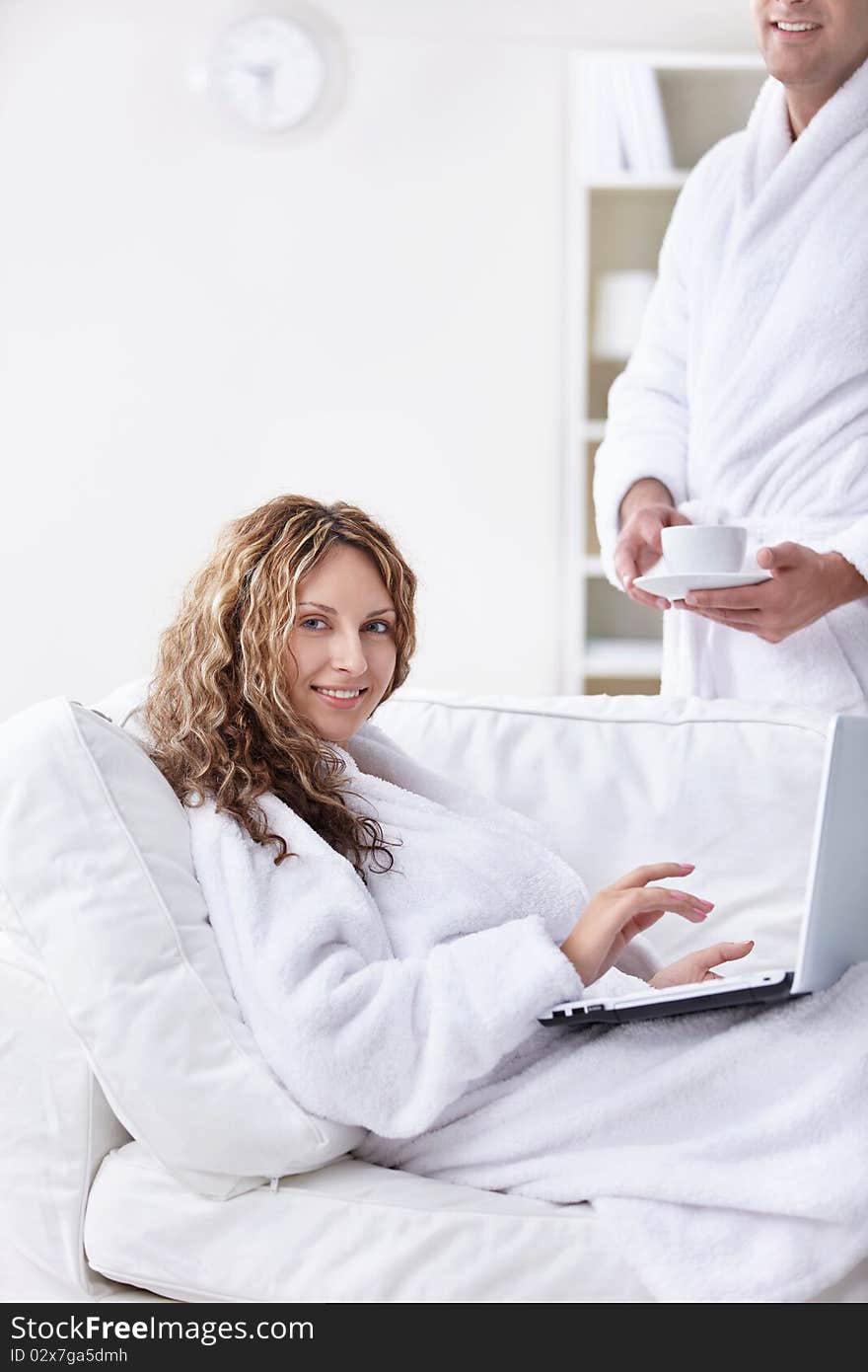 A man in a robe brings coffee girl with laptop. A man in a robe brings coffee girl with laptop