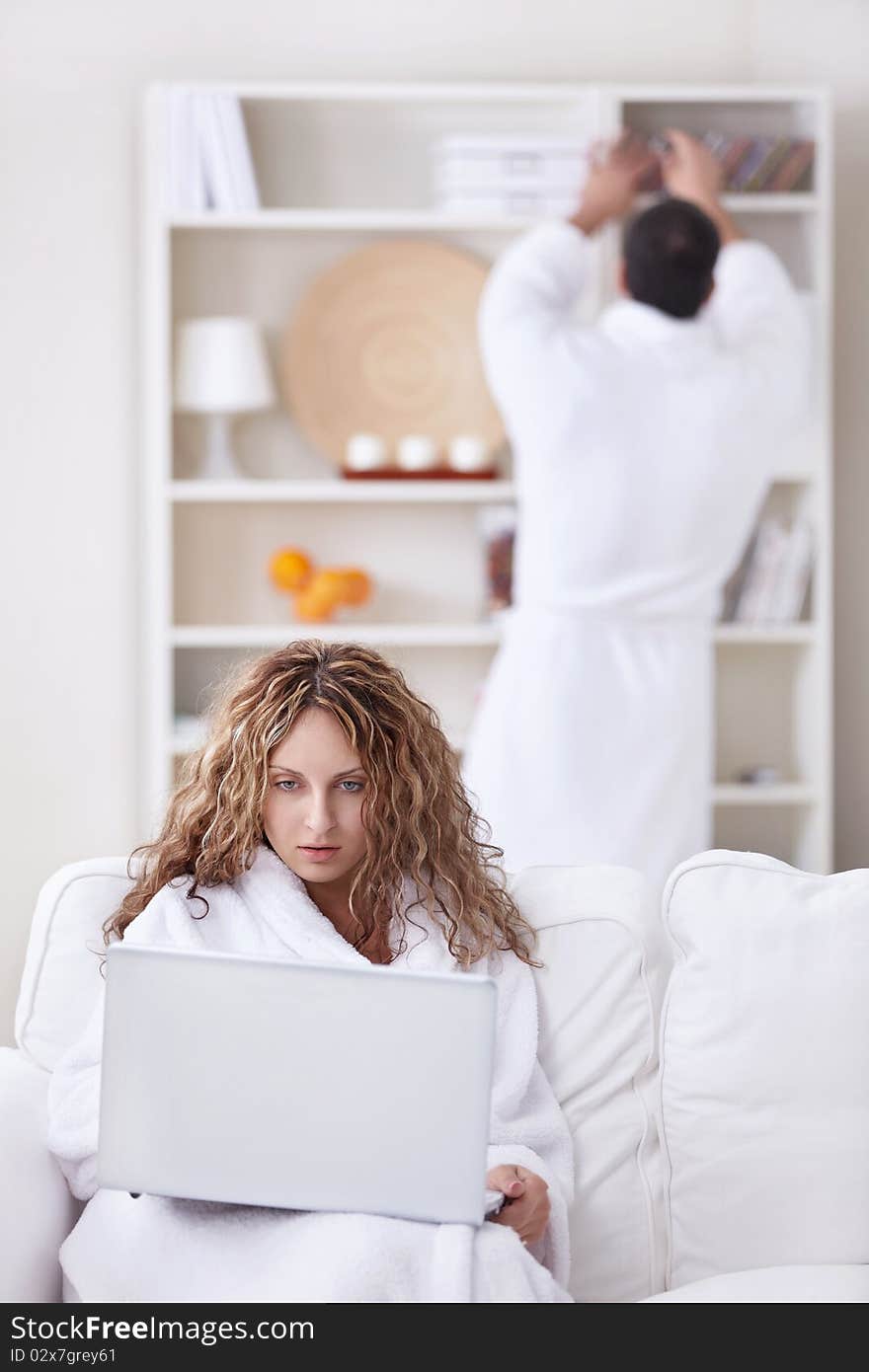 A girl in a bathrobe looking at a laptop in the foreground. A girl in a bathrobe looking at a laptop in the foreground