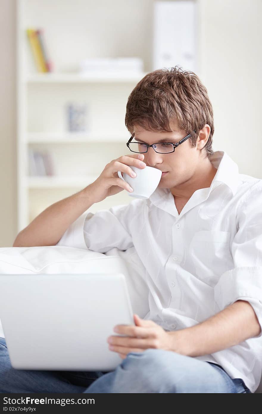 A young man with a cup of looking at the laptop at home. A young man with a cup of looking at the laptop at home