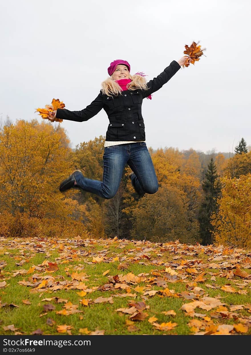 Beautiful girl with autumn leafs in a park jumping