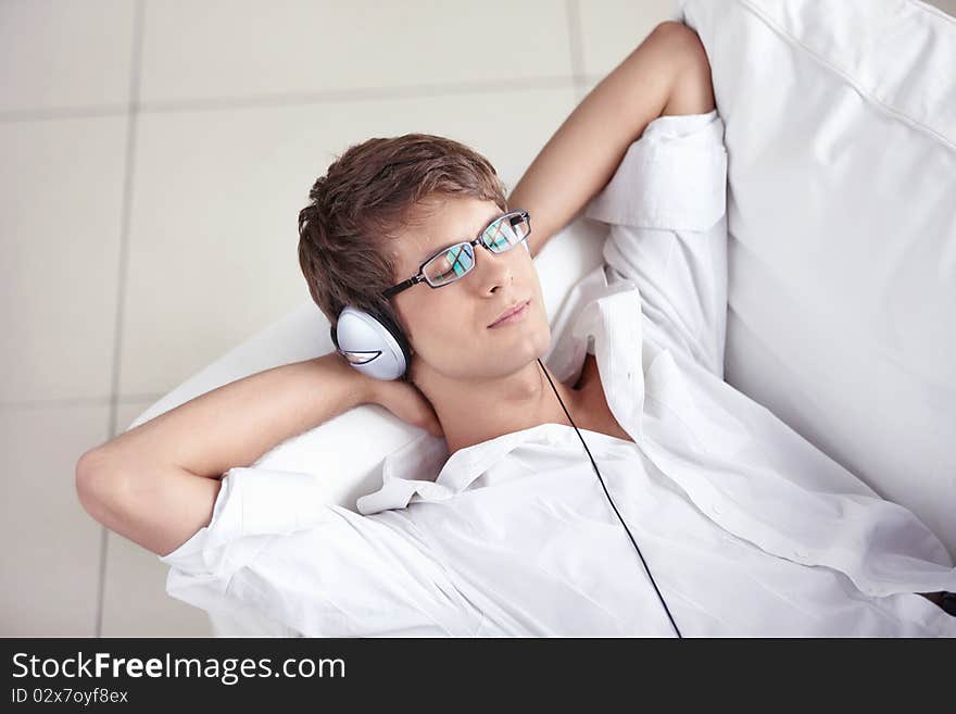 A young man listening the music in the headphones on the sofa. A young man listening the music in the headphones on the sofa