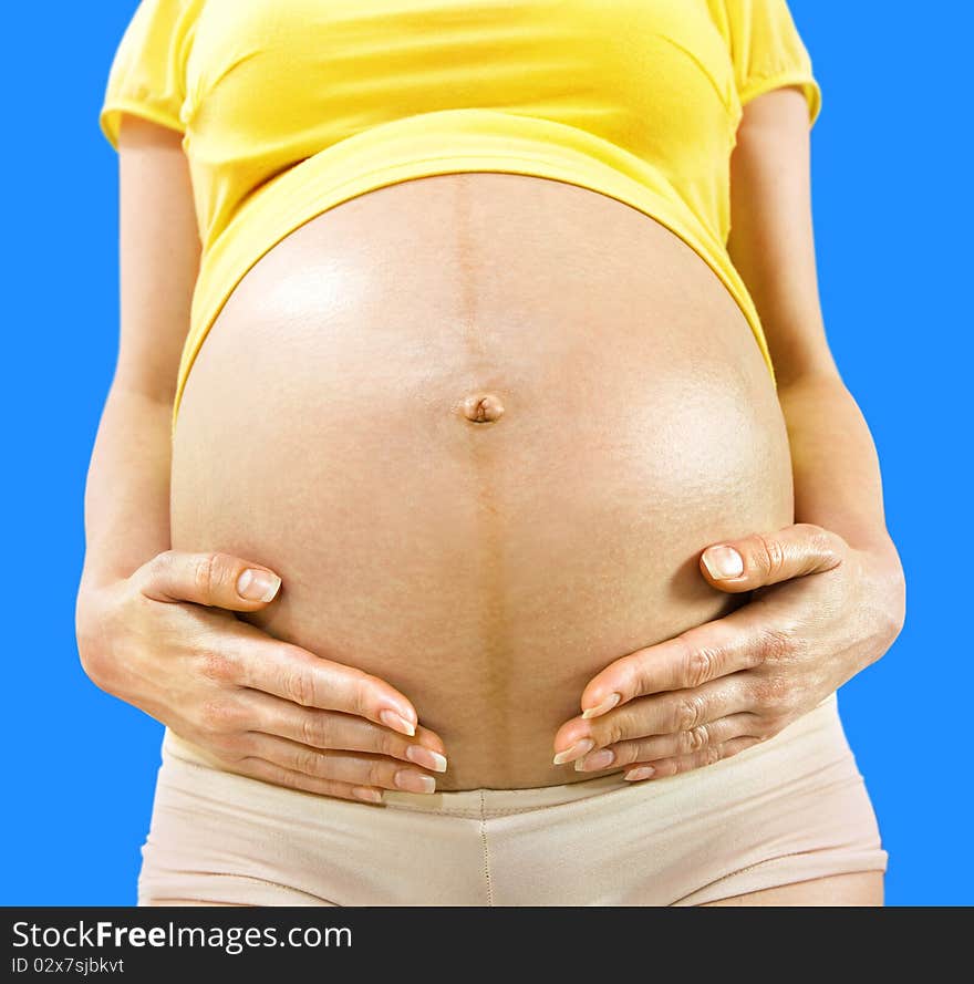 Closeup stomach and hands of pregnant woman on blue background