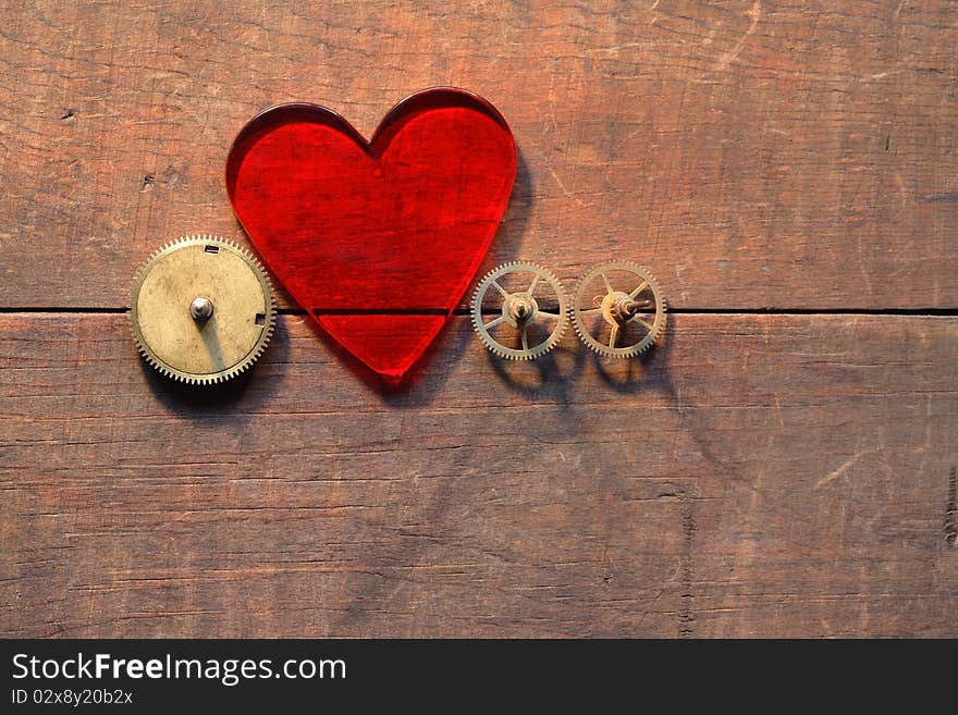 Red glass heart and gears on wooden background. Red glass heart and gears on wooden background